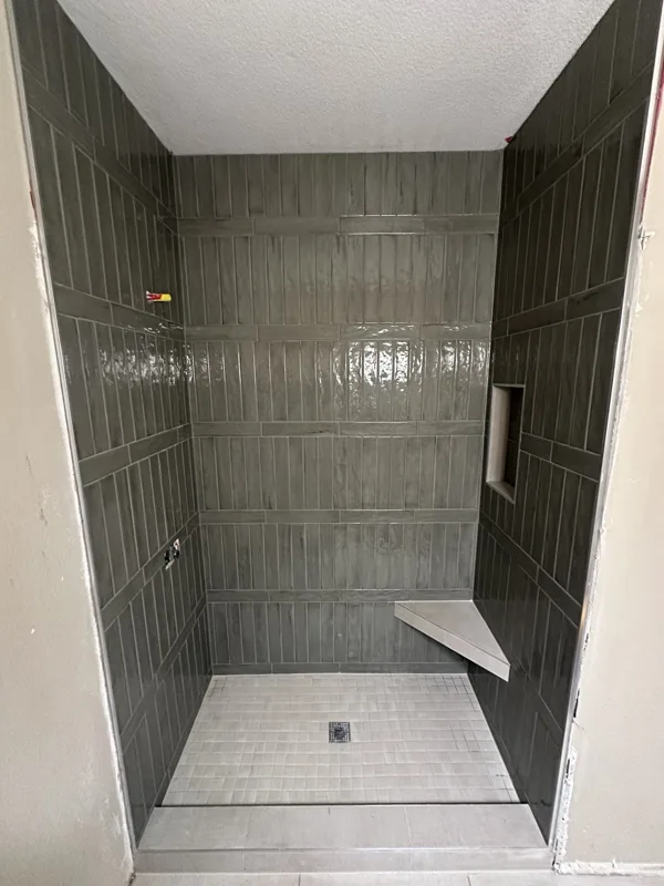 Deep green wall tile, a built-in bench, and a mosaic shower floor.