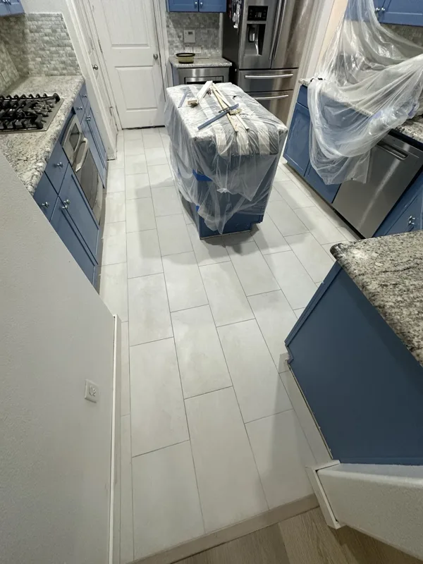 Tile installation underway in a protected kitchen workspace.