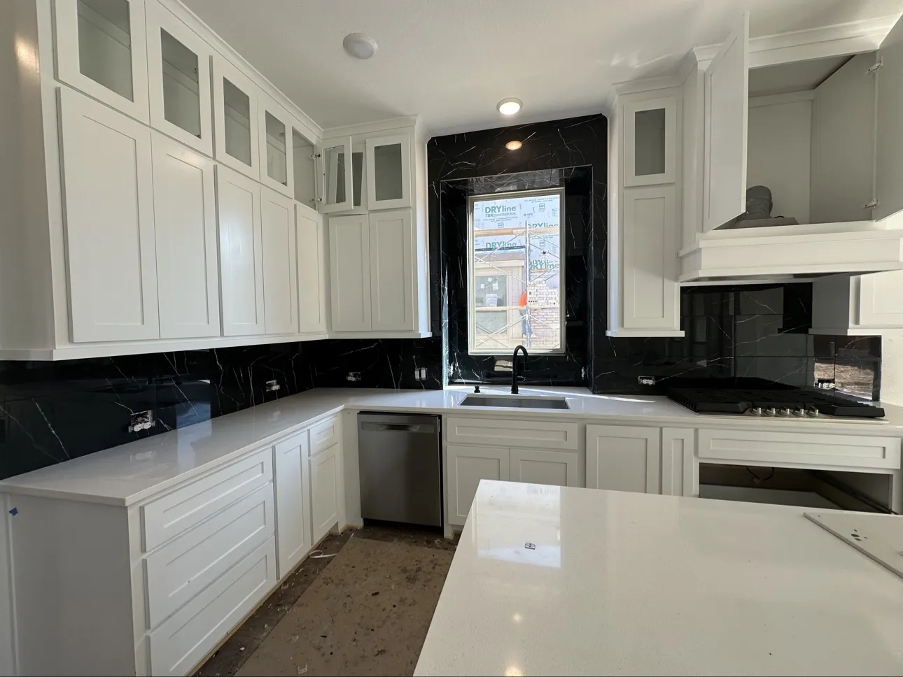 Black marble-look tile backsplash wrapping a kitchen window, with white cabinetry