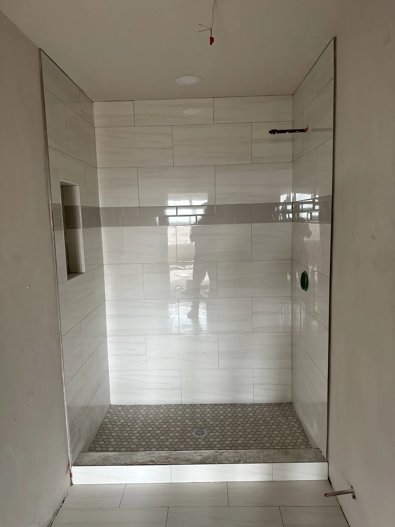Marble-look wall tile with a gray accent band, a built-in niche, and a hex mosaic floor.